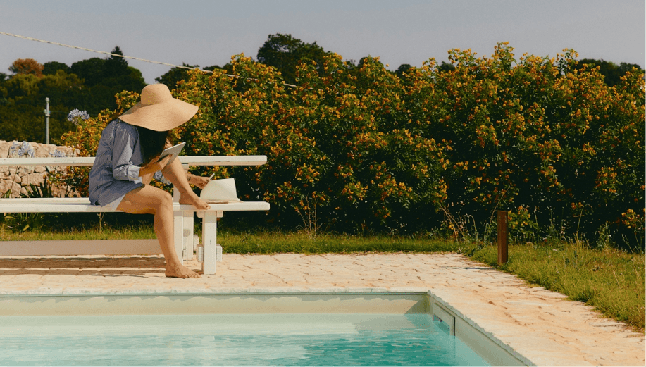 A woman in a sunhat sitting by a pool